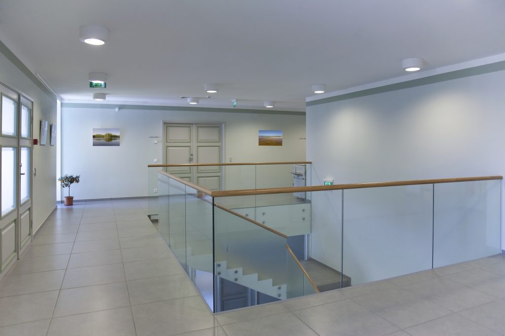 Stairwell and open plan room with large windows and light airy feel, glass balustrade.